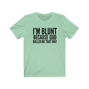 May include: A light green t-shirt with black text that reads "I'm blunt because God rolled me that way."
