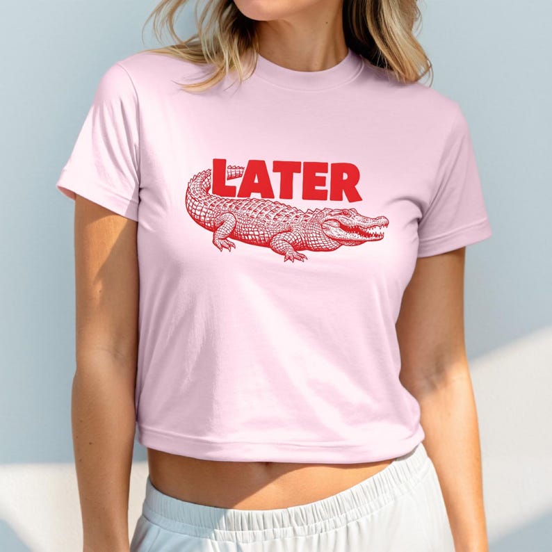 May include: A pink cropped t-shirt with a red alligator graphic and the word "LATER" printed in red.