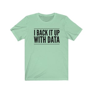May include: A light mint green short-sleeved t-shirt featuring the black text I BACK IT UP WITH DATA centered on the chest. The text is enclosed between two horizontal lines made of small black dots, creating a clean and simple graphic design.