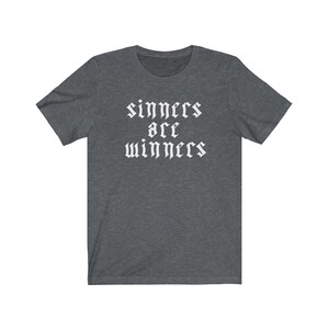 May include: A dark heather grey t-shirt with the text "sinners are winners" printed in white in a gothic font.