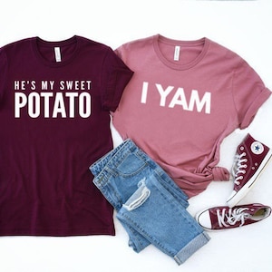 Op de afbeelding: Twee T-shirts met een bijpassend koppelontwerp. Het maronkleurige T-shirt zegt "He's my sweet potato" en het roze T-shirt zegt "I yam".