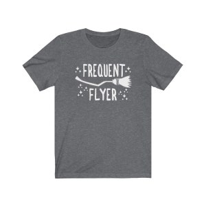May include: A dark heather grey t-shirt with a white graphic of a broom and the text "Frequent Flyer".