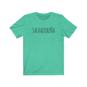 以下が含まれることがあります： 黒で「SALVADORE&Ntilde;A」とプリントされたターコイズグリーンのTシャツです。
