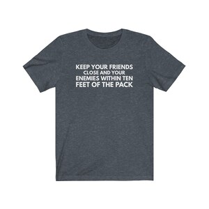 May include: A dark heather gray t-shirt with white text that reads "Keep your friends close and your enemies within ten feet of the pack."