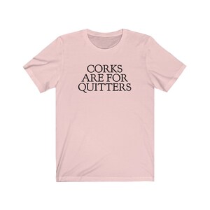 May include: A pink t-shirt with the text "Corks are for quitters" printed in black.