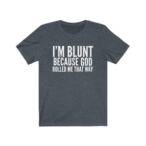May include: Dark grey t-shirt with the white text "I'M BLUNT BECAUSE GOD ROLLED ME THAT WAY". The shirt has short sleeves and a crew neck. The text is centered on the front of the shirt.