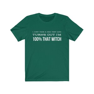 May include: A dark green short-sleeved t-shirt featuring white text printed on the chest that reads: I JUST TOOK A DNA TEST AND TURNS OUT I'M 100% THAT WITCH. The garment has a crew neckline and a standard fit with a solid color background.