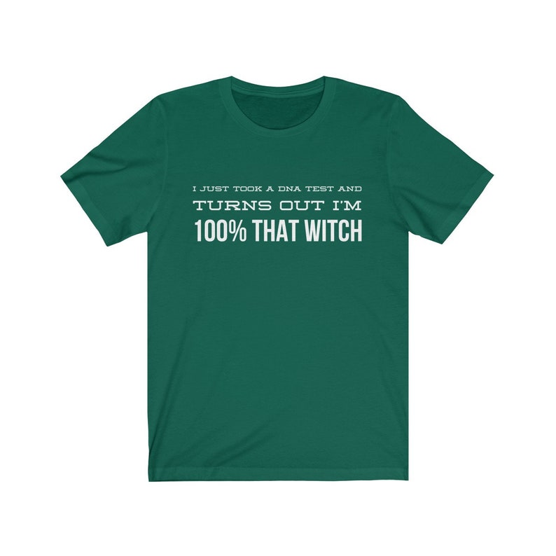 May include: A dark green short-sleeved t-shirt featuring white text printed on the chest that reads: I JUST TOOK A DNA TEST AND TURNS OUT I'M 100% THAT WITCH. The garment has a crew neckline and a standard fit with a solid color background.