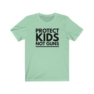 May include: A light green t-shirt with black text that reads "PROTECT KIDS NOT GUNS".