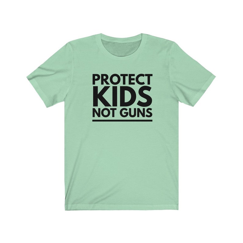 May include: A light green t-shirt with black text that reads "PROTECT KIDS NOT GUNS".