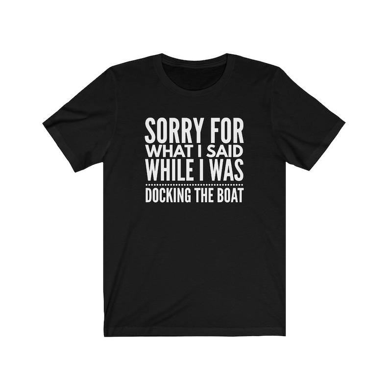 Op de afbeelding: Zwart T-shirt met witte tekst: "SORRY FOR WHAT I SAID WHILE I WAS DOCKING THE BOAT". Het T-shirt heeft een ronde hals en lijkt van een zachte stof te zijn. De tekst is gecentreerd op de voorkant van het kledingstuk.