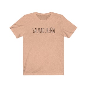 以下が含まれることがあります： 薄いピーチ色のTシャツで、前面に黒い文字で「SALVADORE&Ntilde;A」と印刷されています。