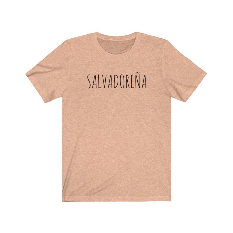 以下が含まれることがあります： 薄いピーチ色のTシャツで、前面に黒い文字で「SALVADORE&Ntilde;A」と印刷されています。