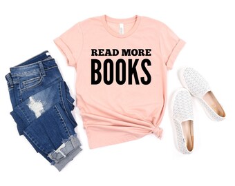 May include: A peach-colored short-sleeve t-shirt with the text READ MORE BOOKS printed in bold black letters, accompanied by a pair of dark blue distressed denim jeans and white slip-on shoes with a subtle textured pattern.