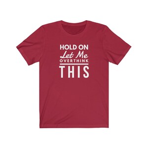 May include: Red short-sleeved t-shirt with white text that reads "Hold On Let Me Overthink This".