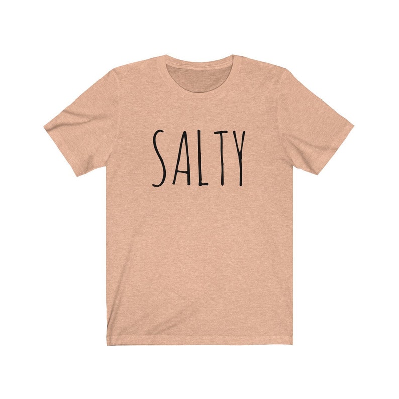 May include: A light peach colored t-shirt with the word "SALTY" printed in black on the front.