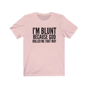 May include: A pink t-shirt with the text "I'M BLUNT BECAUSE GOD ROLLED ME THAT WAY" printed in black.