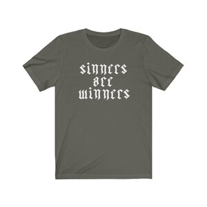 May include: A dark green t-shirt with white text that reads "sinners are winners" in a gothic font.