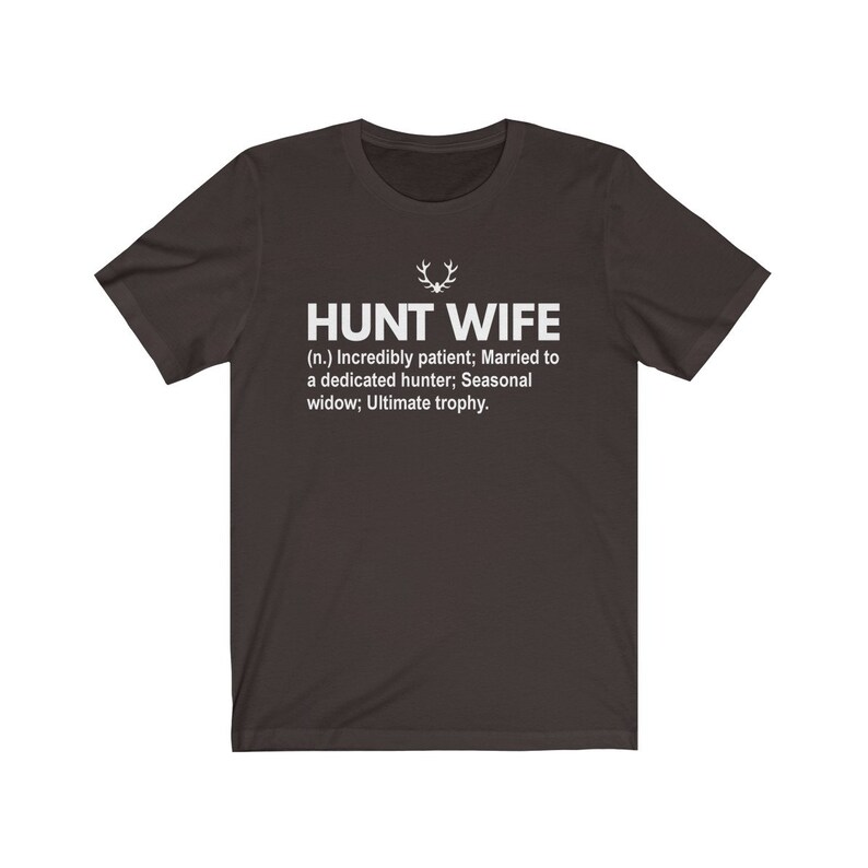 May include: A dark gray t-shirt with white text that reads "HUNT WIFE (n.) Incredibly patient; Married to a dedicated hunter; Seasonal widow; Ultimate trophy."