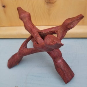 May include: A wooden stand with three legs, made of dark red wood. The stand is designed to hold a crystal or other object.