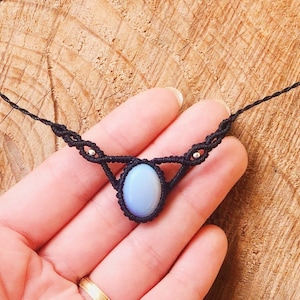 Könnte beinhalten: Eine zarte schwarze Makramee-Halskette mit einem hellblauen ovalen Edelstein-Anhänger.