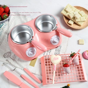 May include: Pink electric chocolate fondue fountain with two dipping pots, four dipping forks, a pink gridded tray, and a white chocolate lollipop. The fondue fountain has two knobs labelled "Chocolate".