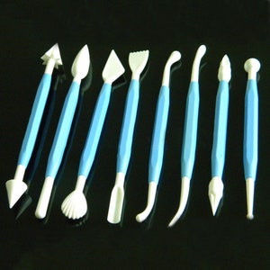 Puede incluir: Conjunto de diez herramientas de plástico azul y blanco para esculpir y decorar fondant o pasta de goma. Las herramientas tienen varias formas, incluyendo una hoja, una flor, una concha y una bola.