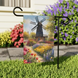 May include: A colorful garden flag with a painting of a windmill in a field of flowers. The windmill is blue and brown with white blades. The flowers are yellow, pink, purple, and red.