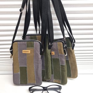 Könnte beinhalten: Vier rechteckige Umhängetaschen mit Patchwork-Designs in Grau-, Olivgrün- und Brauntönen. Jede Tasche hat einen schwarzen, verstellbaren Riemen und ein kleines Etikett mit der Aufschrift "BY SIENE". Eine schwarze Brille mit rosa Rand befindet sich im Vordergrund.