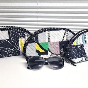 Könnte beinhalten: Drei schwarze und weiße gemusterte Kosmetiktaschen aus Stoff mit schwarzem Besatz und eine schwarze Sonnenbrille.