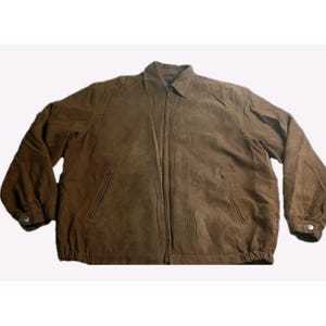 May include: A brown suede jacket with a full zipper closure, two front pockets, and buttoned cuffs. The jacket has a collared neckline and a slightly gathered hemline. The overall style is casual and classic.