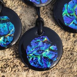 May include: Three black round pendants with a blue, green, and iridescent design. The pendants are on a black cord.