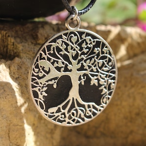 May include: A silver tree of life pendant necklace with a black background. The pendant is round and has intricate details.