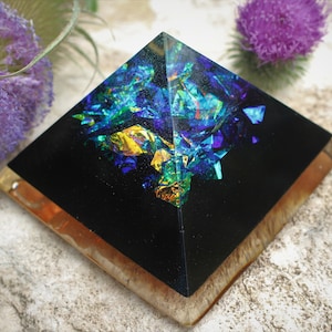 May include: A black resin pyramid with iridescent blue, green, and gold glitter embedded inside. The pyramid is sitting on a wooden base.