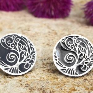May include: A pair of silver earrings with a black enamel background and a detailed silver tree design.
