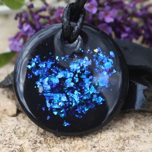 May include: A black pendant with a blue glitter design. The pendant is round and has a black cord.