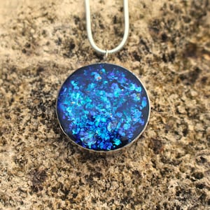 May include: A silver chain necklace with a round pendant featuring blue and teal glitter embedded in clear resin.