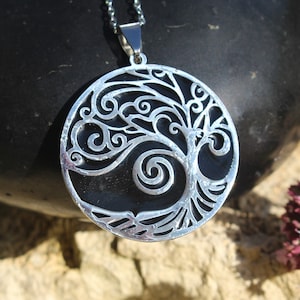 May include: A silver pendant necklace featuring a tree of life design with intricate swirls and a black background.