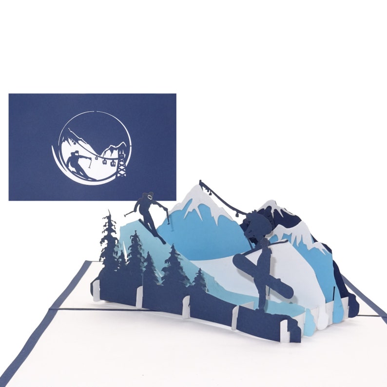 May include: A blue and white paper pop-up card with a winter scene. The card features a mountain range with skiers and snowboarders. The card is open and the pop-up is fully extended. The card is on a white background.