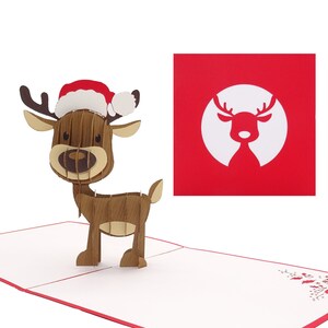 May include: A 3D pop-up card featuring a reindeer wearing a red and white Santa hat. The card is open and the reindeer is standing on a white background. The card has a red border and a small holly sprig in the bottom right corner.