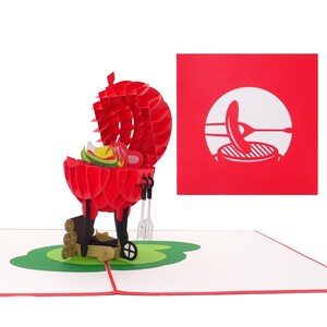Puede incluir: Una tarjeta pop-up 3D roja y negra que representa una barbacoa con la tapa abierta, revelando una salchicha, pimientos y cebollas. La barbacoa tiene un juego de pinzas y una esp&aacute;tula. Hay troncos de madera junto a la barbacoa. La tarjeta est&aacute; sobre una base verde y tiene un fondo rojo con una silueta blanca de una barbacoa con una salchicha encima.