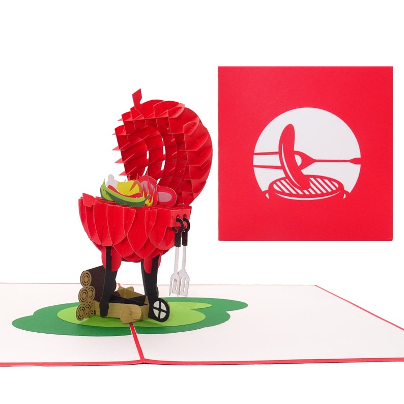 Puede incluir: Una tarjeta pop-up 3D roja y negra que representa una barbacoa con la tapa abierta, revelando una salchicha, pimientos y cebollas. La barbacoa tiene un juego de pinzas y una esp&aacute;tula. Hay troncos de madera junto a la barbacoa. La tarjeta est&aacute; sobre una base verde y tiene un fondo rojo con una silueta blanca de una barbacoa con una salchicha encima.