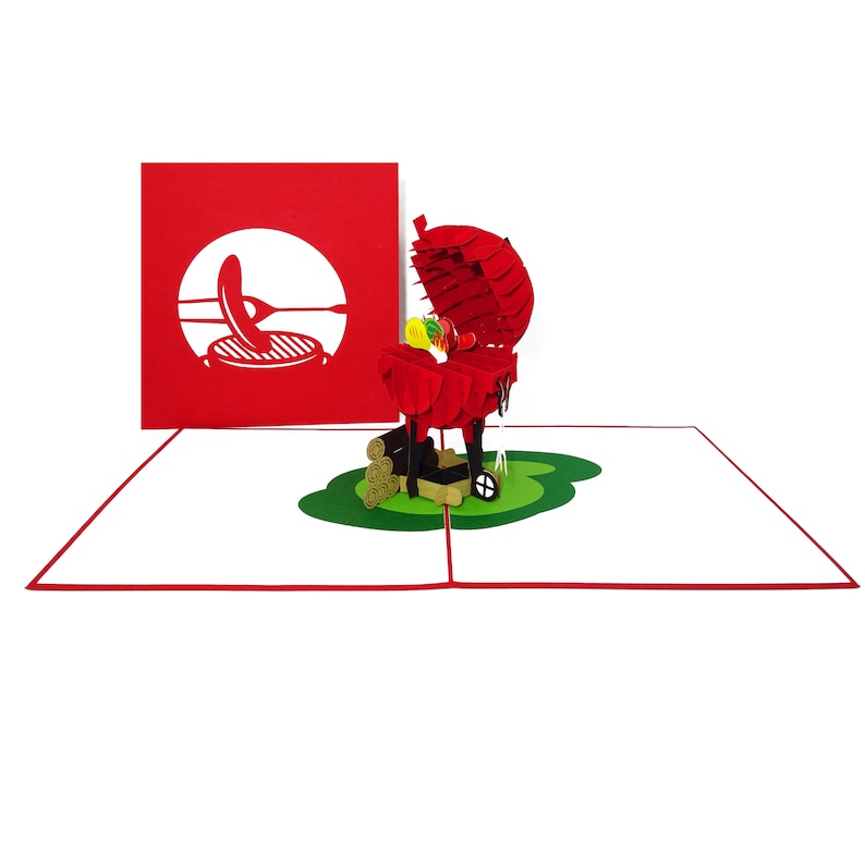 Puede incluir: Una tarjeta pop-up 3D roja que representa una barbacoa con comida cocin&aacute;ndose en su interior. La barbacoa est&aacute; sobre un c&eacute;sped verde con troncos de madera cerca. La tarjeta est&aacute; cerrada y muestra una silueta roja de una barbacoa con una esp&aacute;tula y un filete.
