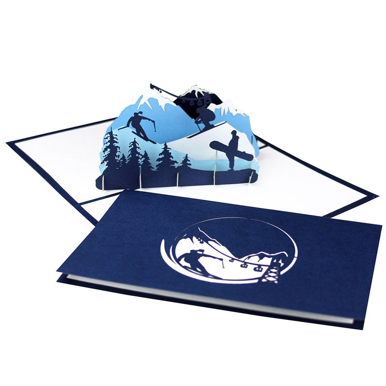 May include: A blue pop-up card with a 3D scene of skiers and snowboarders on a mountain. The card is closed and the front shows a silhouette of the scene.
