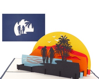 May include: A 3D pop-up card depicting a family of three walking on a beach at sunset. The card is made of paper and features a layered design with a yellow sun, orange and red mountains, blue water, and palm trees.