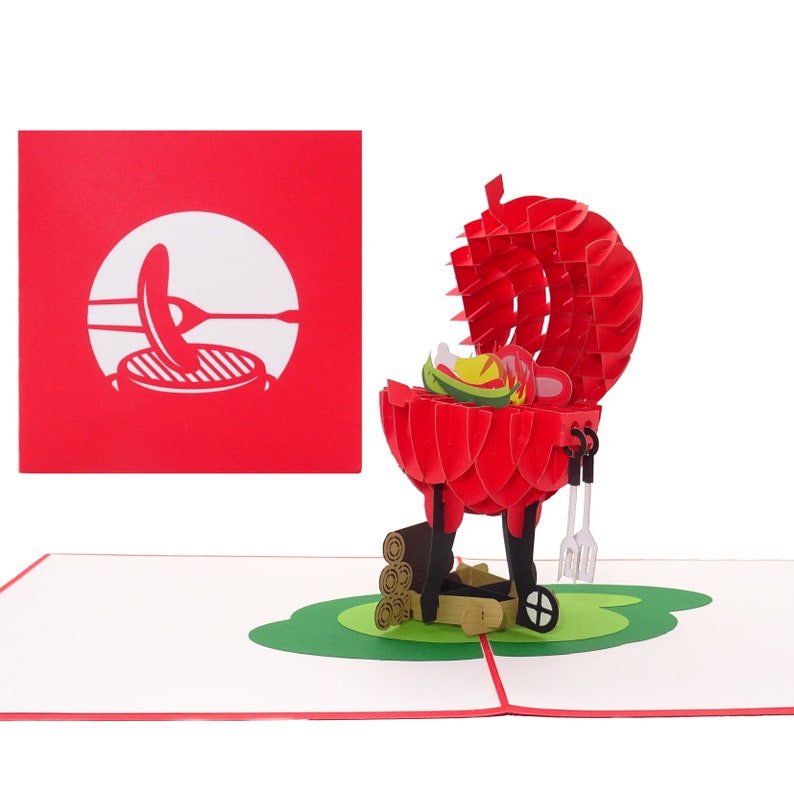 Puede incluir: Una tarjeta pop-up 3D roja que representa una barbacoa con la tapa abierta y comida en su interior. La barbacoa est&aacute; sobre una base verde con troncos de madera debajo. La tarjeta est&aacute; cerrada y muestra una silueta blanca de una barbacoa con una salchicha en una brocheta.