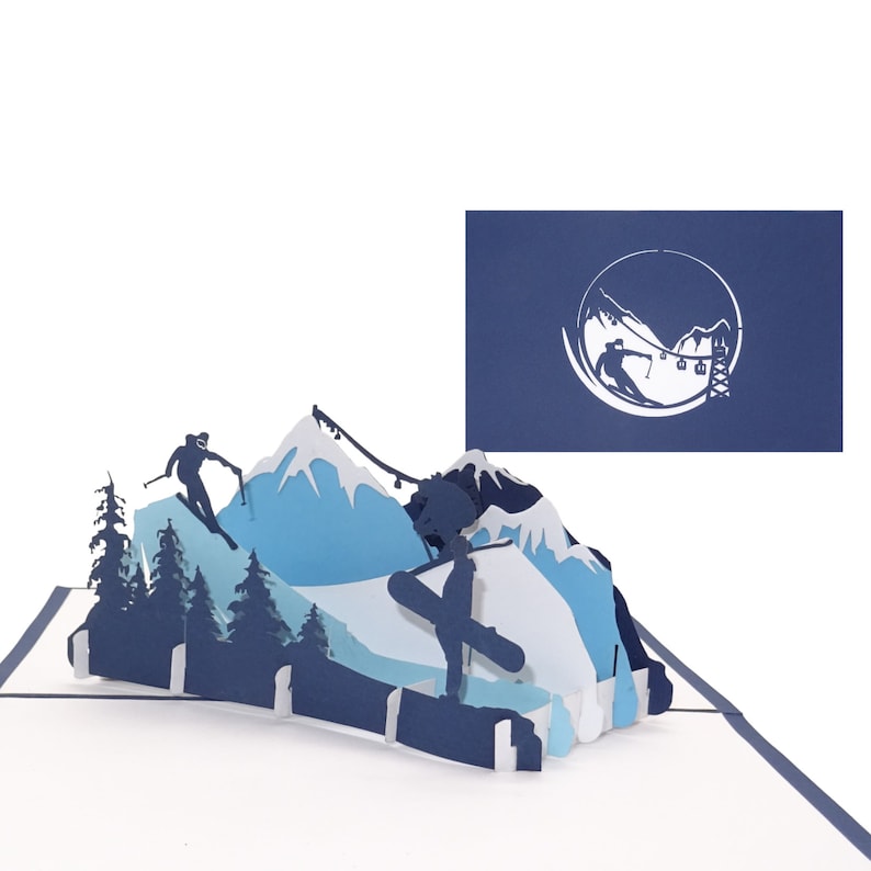 May include: A blue and white paper pop-up card depicting a winter mountain scene with skiers and snowboarders. The card is open and the pop-up is fully extended. The card features a blue background with white mountains and a skier and snowboarder silhouette.