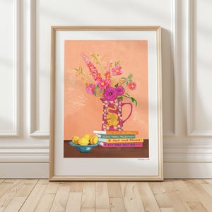 Può includere: Un arrangiamento floreale rosa e bianco in un'anfora rosa con un disegno di tigre. L'anfora è appoggiata su una pila di libri con i titoli "NO RIN NA MAGIL", "GOOD TIMES ARE COMING", "OWN YOUR POWER!" e "LET THAT SHIT GO". Ci sono tre limoni gialli in una ciotola blu su una superficie di legno.