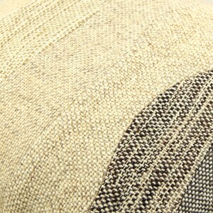 Op de afbeelding: Close-up van een getextureerd kussen met een patchwork ontwerp. Het kussen heeft secties van beige en bruin geweven stof, waardoor een neutrale en aardse esthetiek ontstaat. De weefsel is zichtbaar en voegt diepte toe.