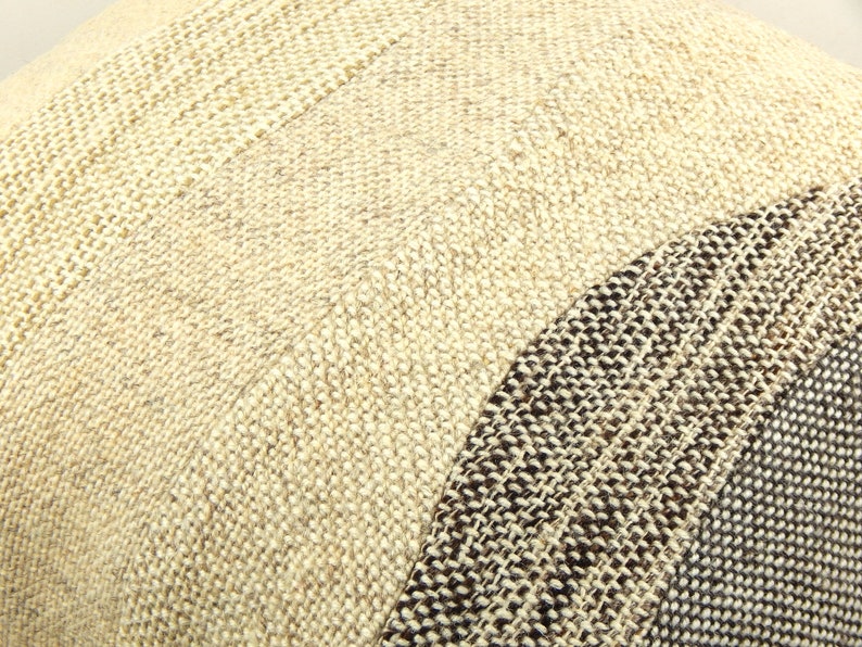 Op de afbeelding: Close-up van een getextureerd kussen met een patchwork ontwerp. Het kussen heeft secties van beige en bruin geweven stof, waardoor een neutrale en aardse esthetiek ontstaat. De weefsel is zichtbaar en voegt diepte toe.